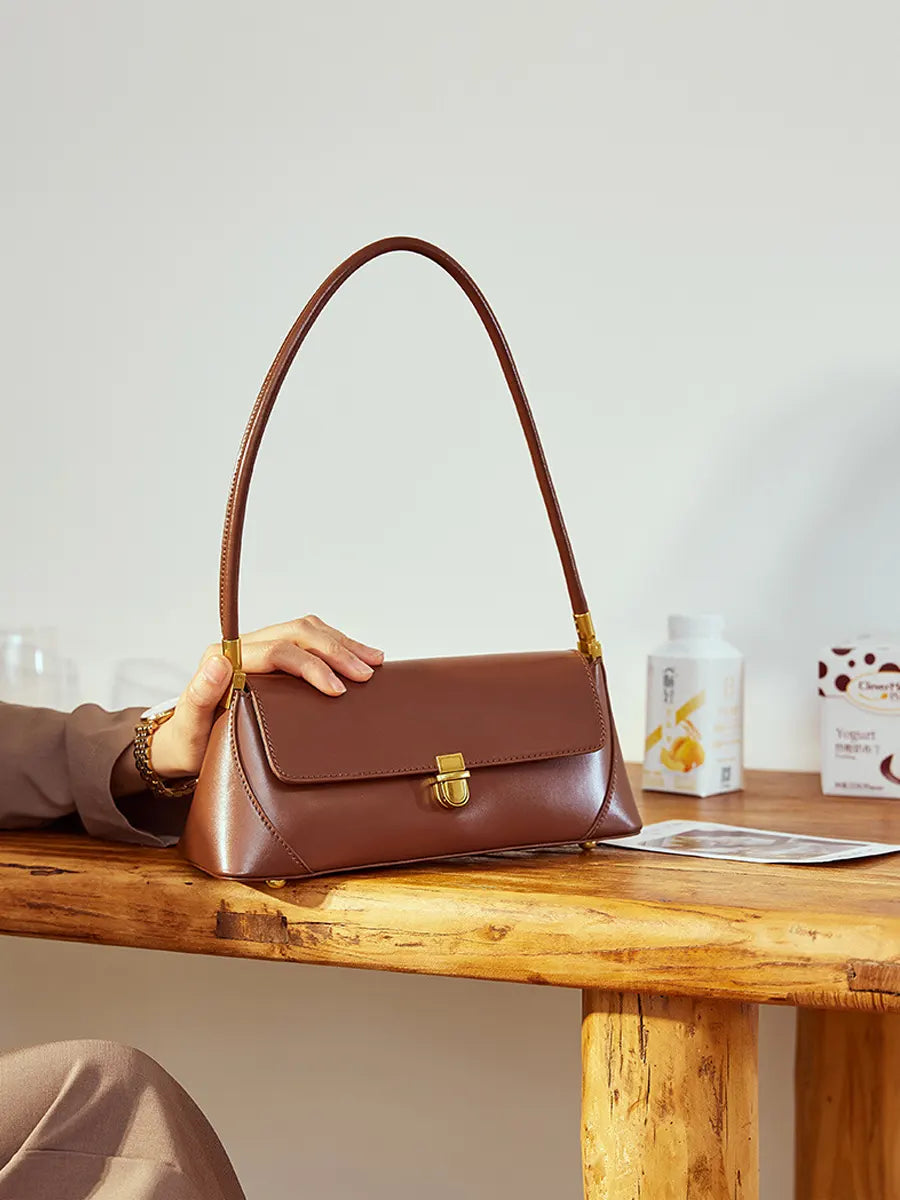 Brown handbag held by a person on a wooden table with a neutral background