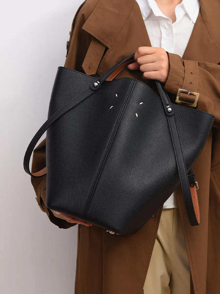 Person holding a black leather bag against a neutral background