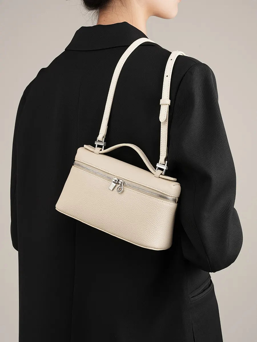 Beige handbag worn over the shoulder by a person in a black outfit on a neutral background