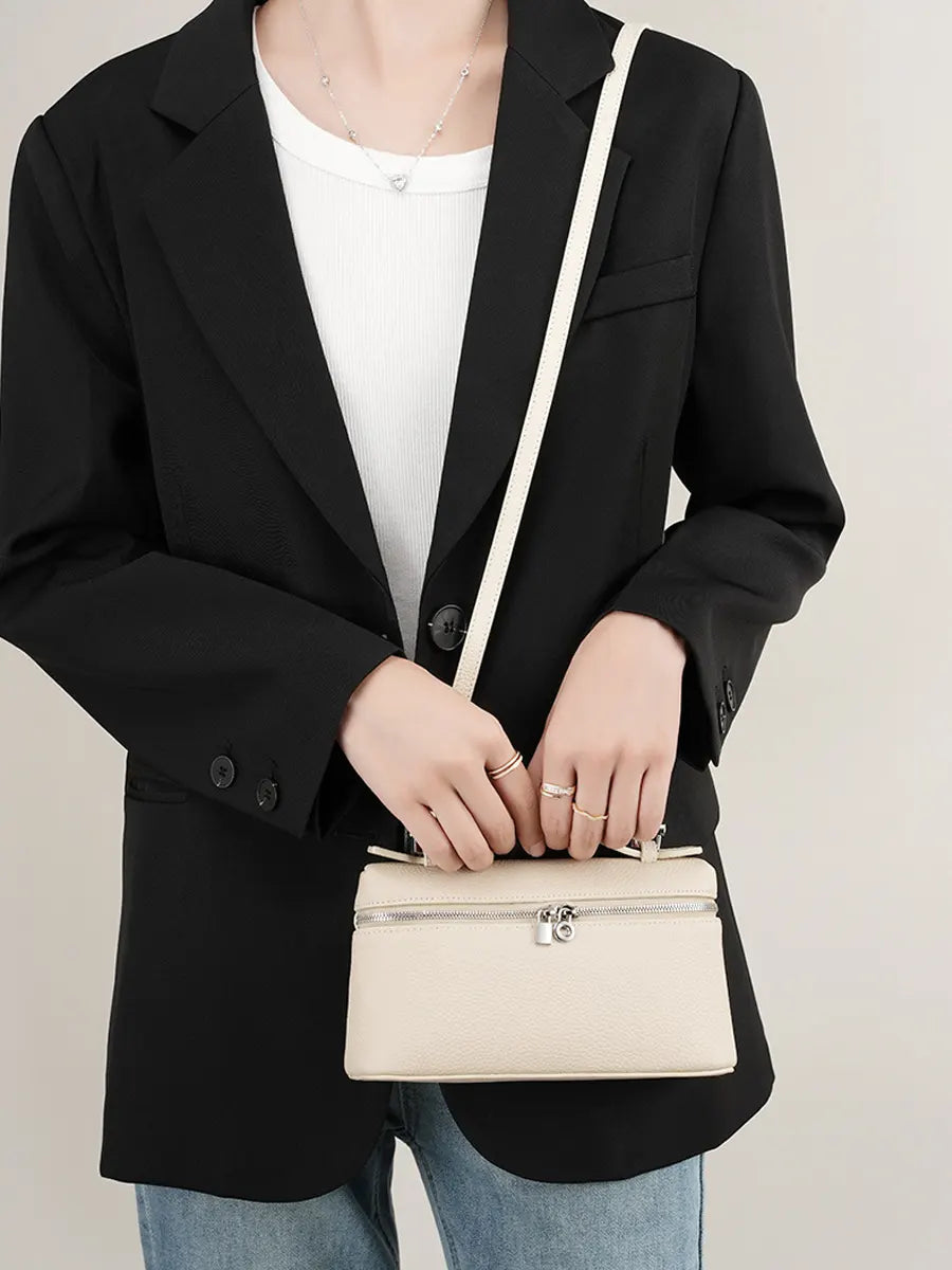Person wearing a black blazer holding a beige handbag against a neutral background