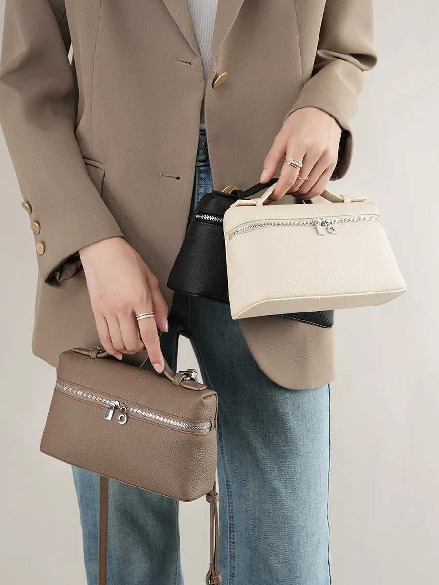 Person holding two handbags, one beige and one brown, against a neutral background