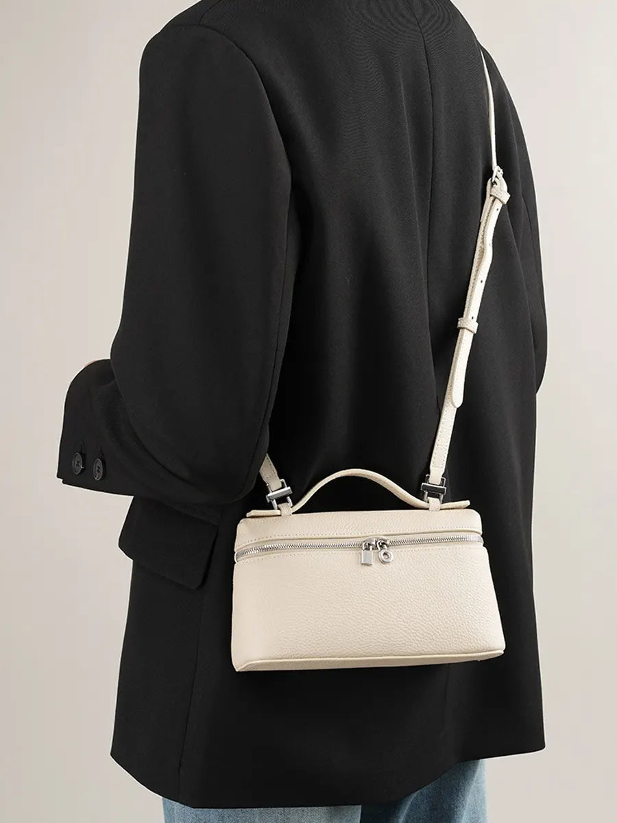 Person wearing a black coat with a white handbag over their shoulder on a plain background