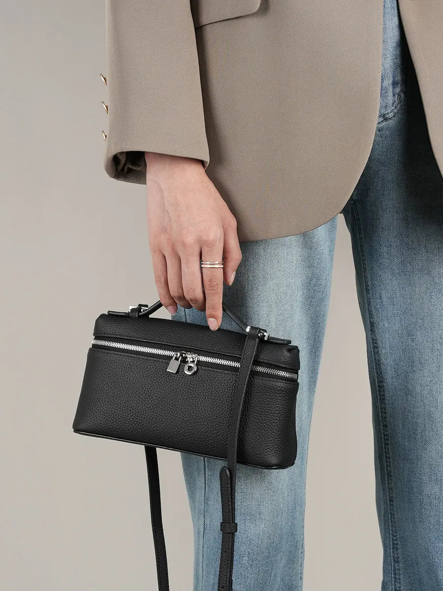 Person holding a black handbag with a neutral background