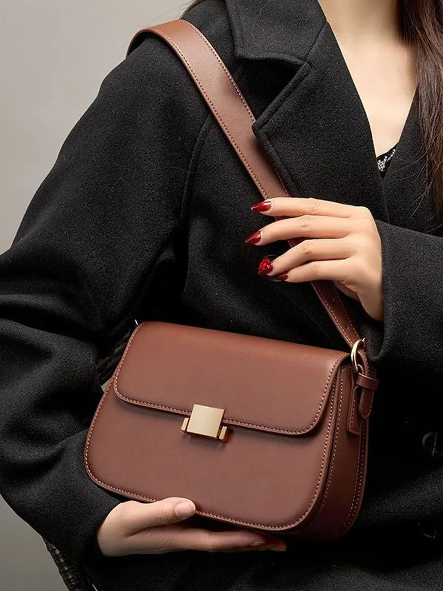 Brown leather handbag held by a person wearing a black coat against a neutral background