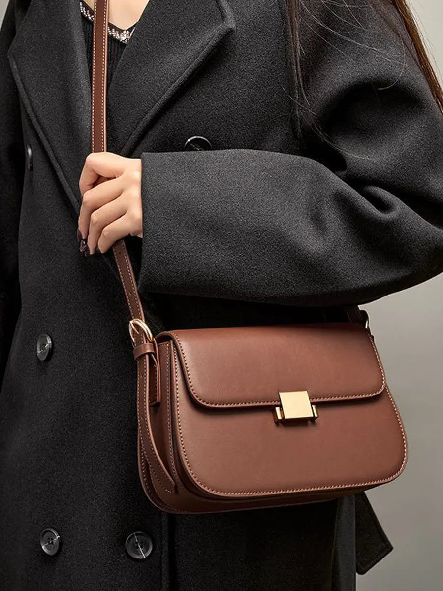Brown leather handbag held by a person wearing a dark coat.