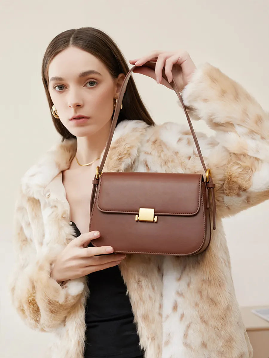 Woman holding a brown handbag wearing a fur coat against a neutral background