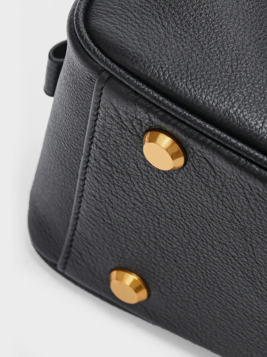 Black leather bag with gold studs on a light gray background