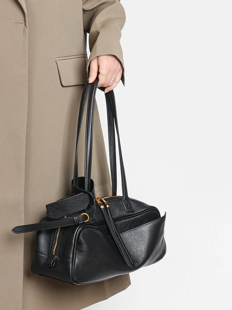 Person holding a black handbag with a neutral background