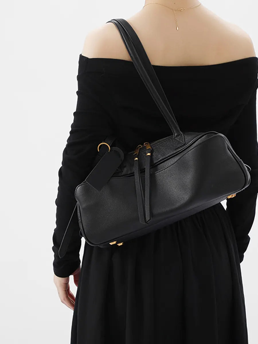 Person wearing a black off-shoulder top and holding a matching black handbag against a white background