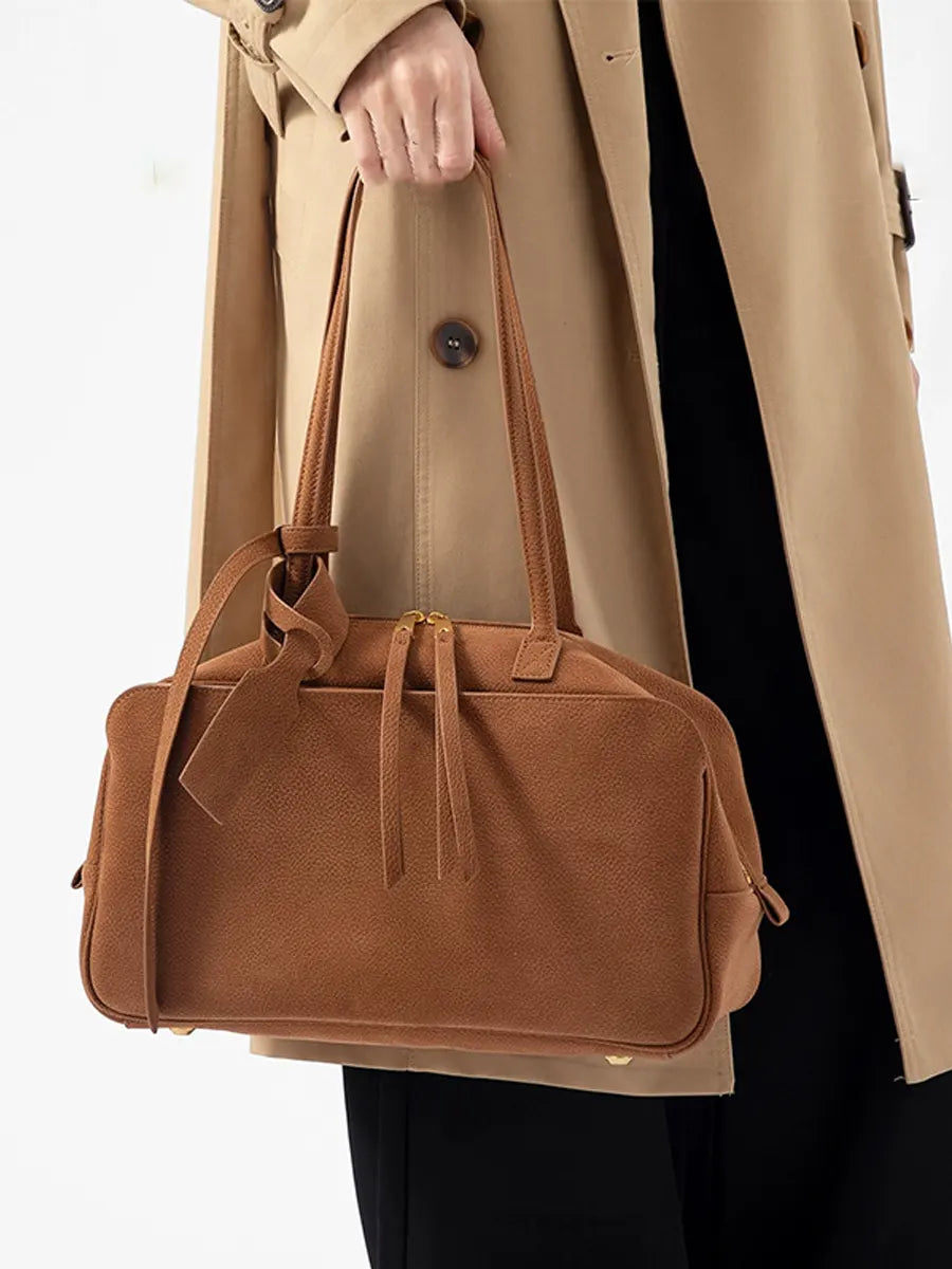Brown handbag held by a person wearing a beige coat on a white background