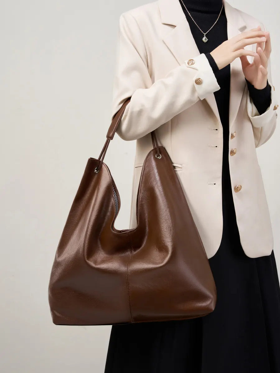 Person holding a brown leather handbag against a neutral background