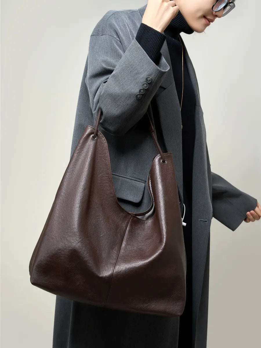 Person holding a brown leather handbag against a plain background