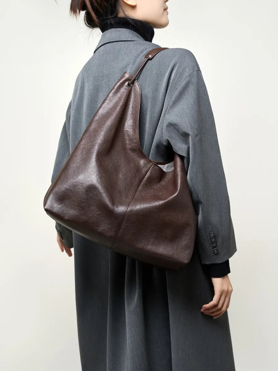 Person wearing a large brown leather bag over one shoulder against a plain background