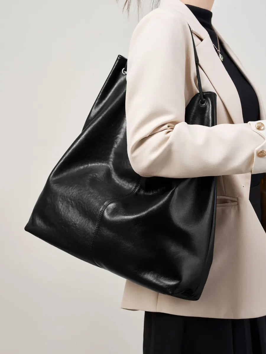 Person holding a black leather tote bag against a neutral background