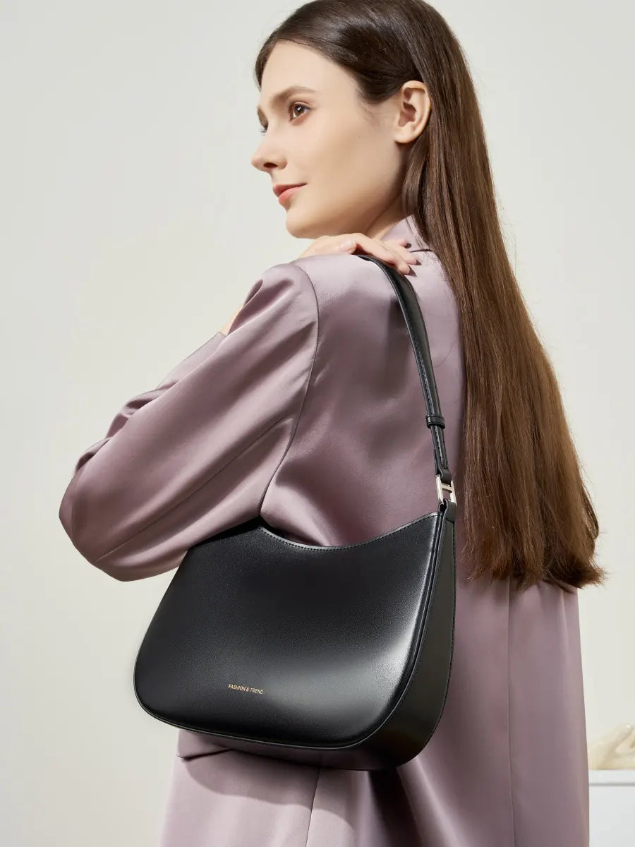 Woman wearing a black shoulder bag against a plain background