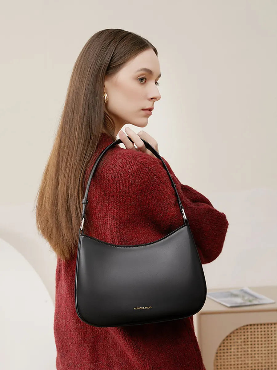Woman wearing a black handbag over her shoulder against a neutral background