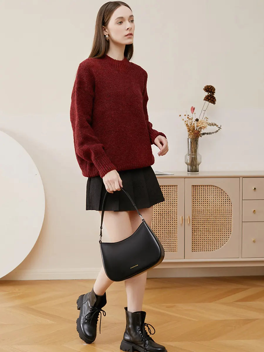 Woman in a red sweater and black skirt holding a black handbag in a room with a cabinet and decorative items.