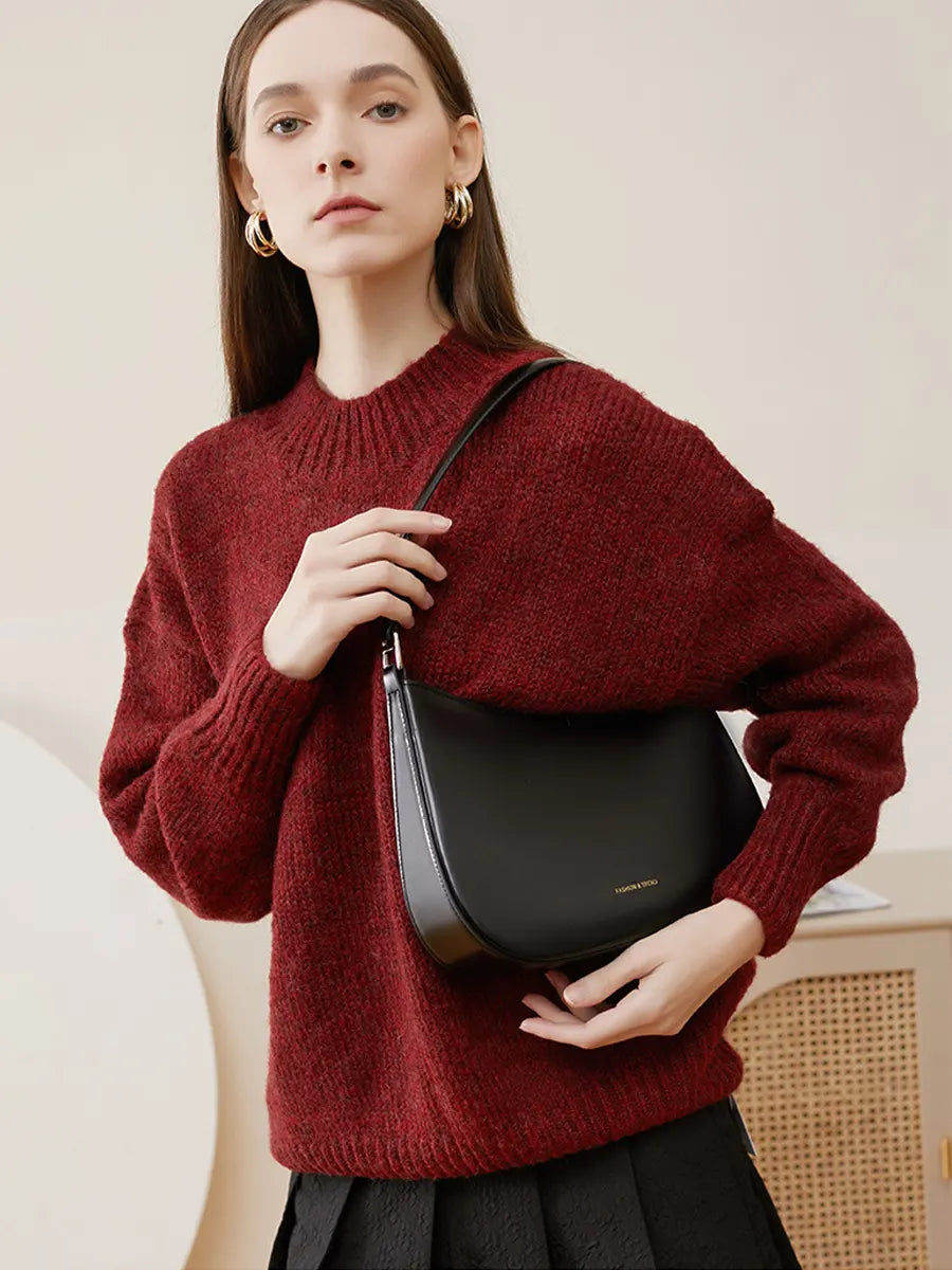 Woman wearing a red sweater holding a black handbag against a neutral background
