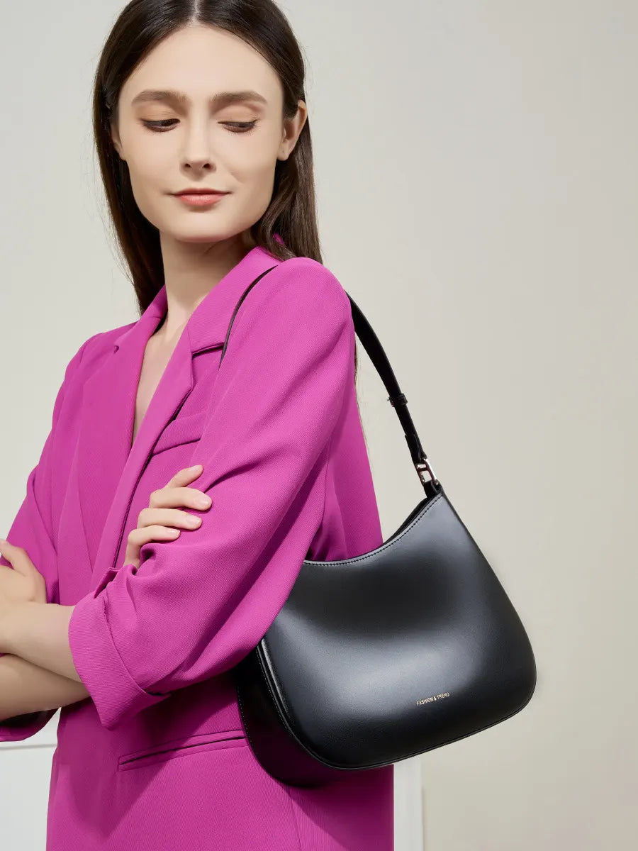 Woman in a pink outfit holding a black handbag against a neutral background
