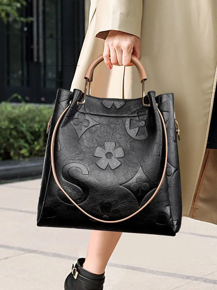 Person holding a black handbag with floral designs on a blurred outdoor background
