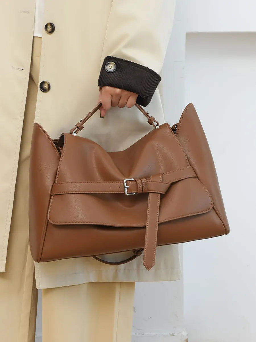Brown leather handbag held by a person wearing a beige coat.