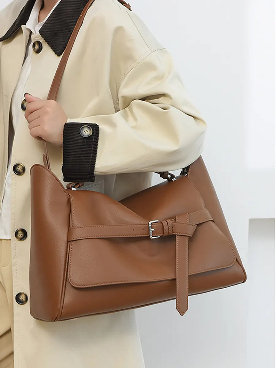 Brown leather handbag held by a person wearing a beige coat on a light gray background