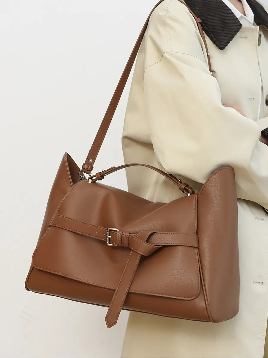 Brown leather handbag worn over the shoulder on a plain background