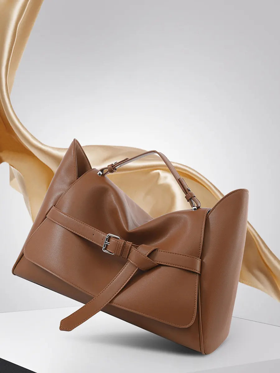 Brown leather handbag on a white surface with a blurred background