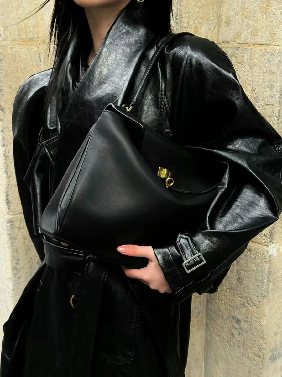 Person holding a black leather handbag against a stone wall background
