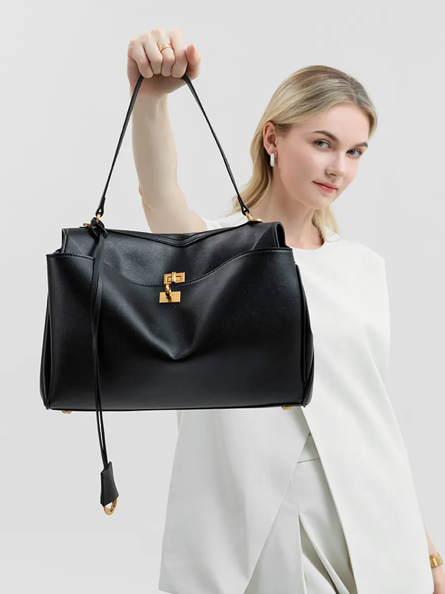 Woman holding a black handbag with a gold clasp against a light gray background