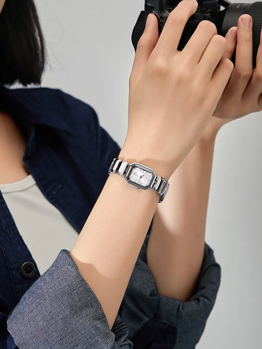 Person wearing a silver watch on a plain background