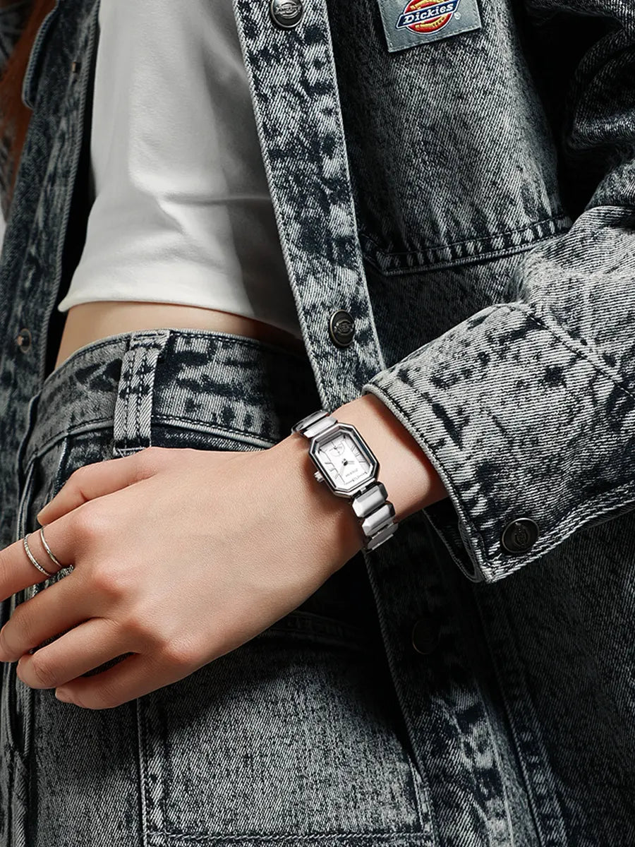 Person wearing a silver watch on a denim jacket with a visible brand logo.