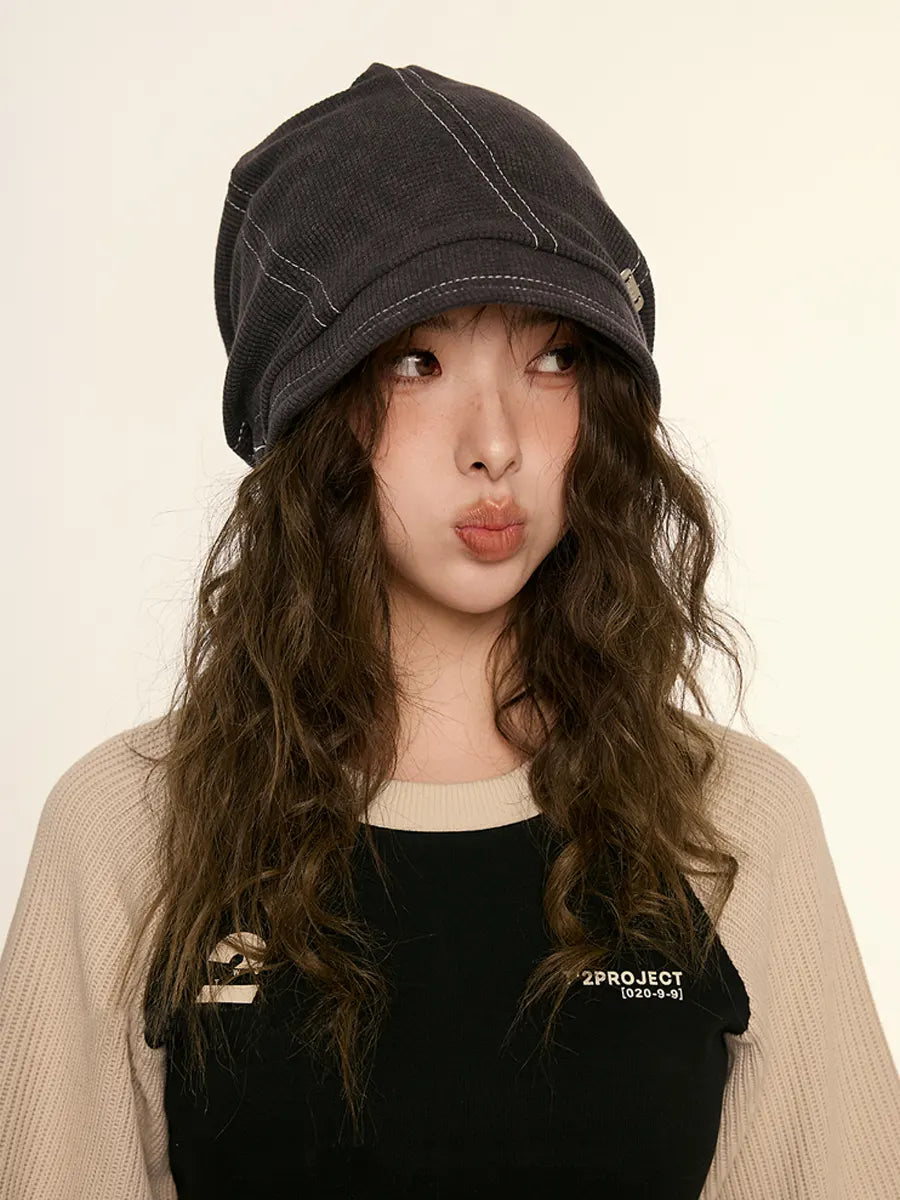 Person wearing a black denim cap and black shirt with '2PROJECT' logo on a beige background