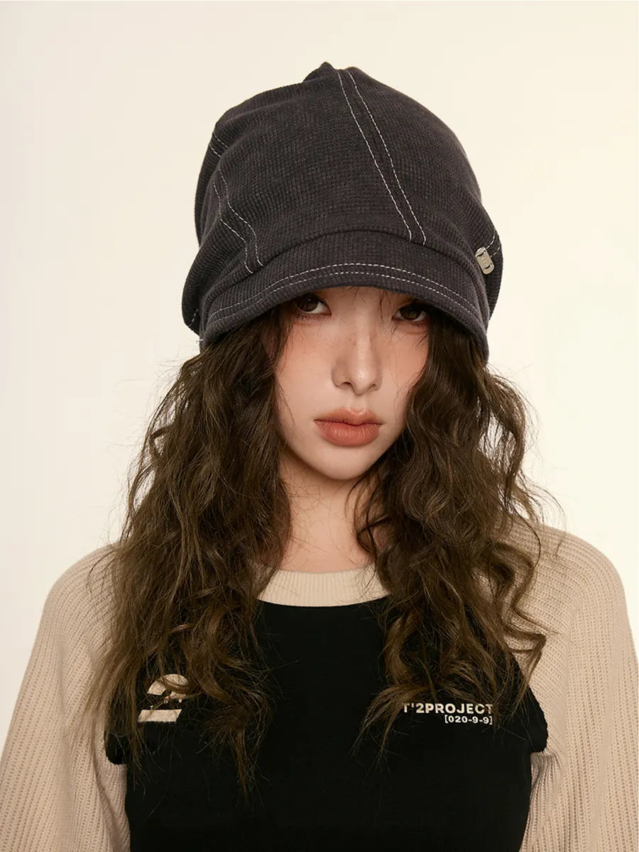 Person wearing a dark denim cap and black top with visible branding on a beige background