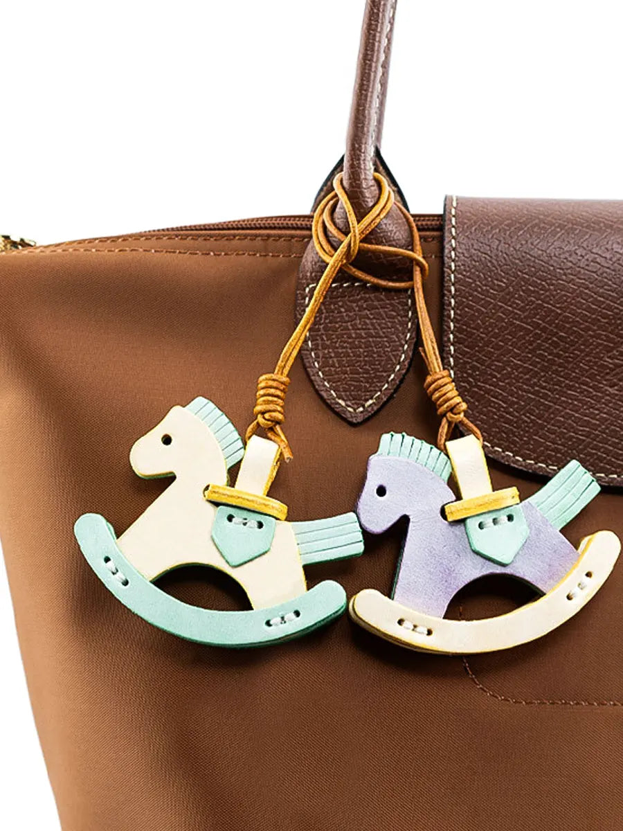 Two wooden rocking horse keychains hanging from a brown leather bag.