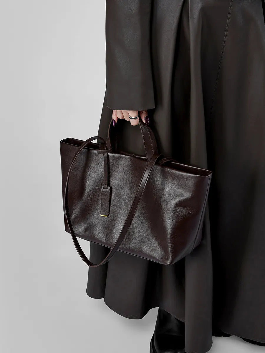 Person holding a brown leather tote bag against a plain background