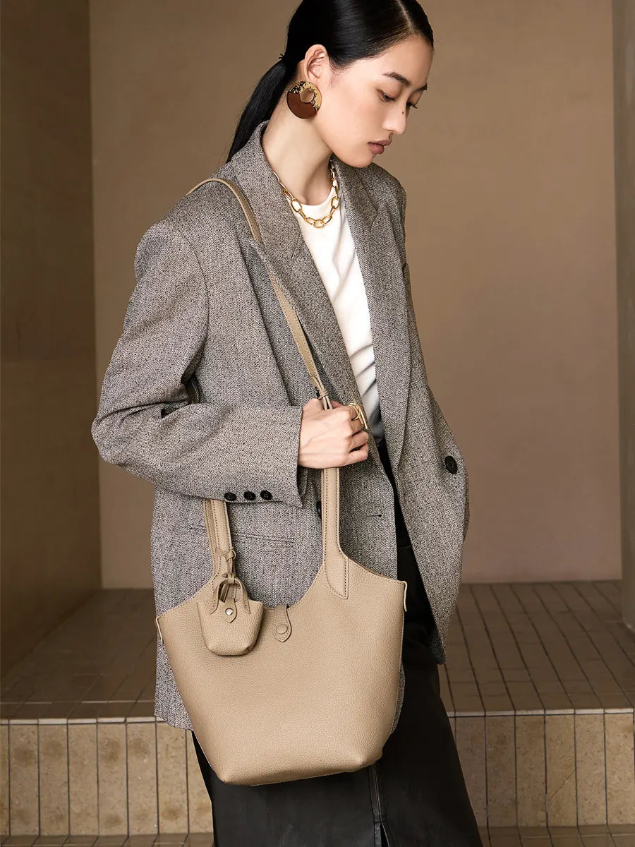Woman holding a beige handbag against a neutral background
