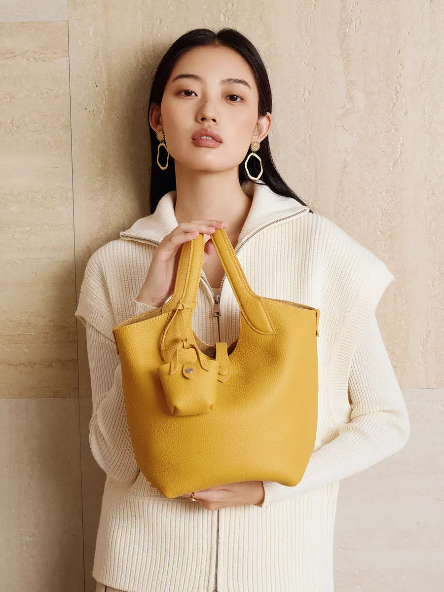 Woman holding a yellow handbag against a beige wall