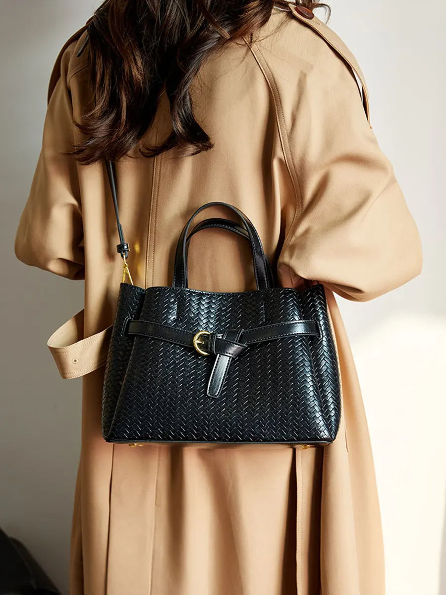 Person wearing a beige coat holding a black woven handbag.
