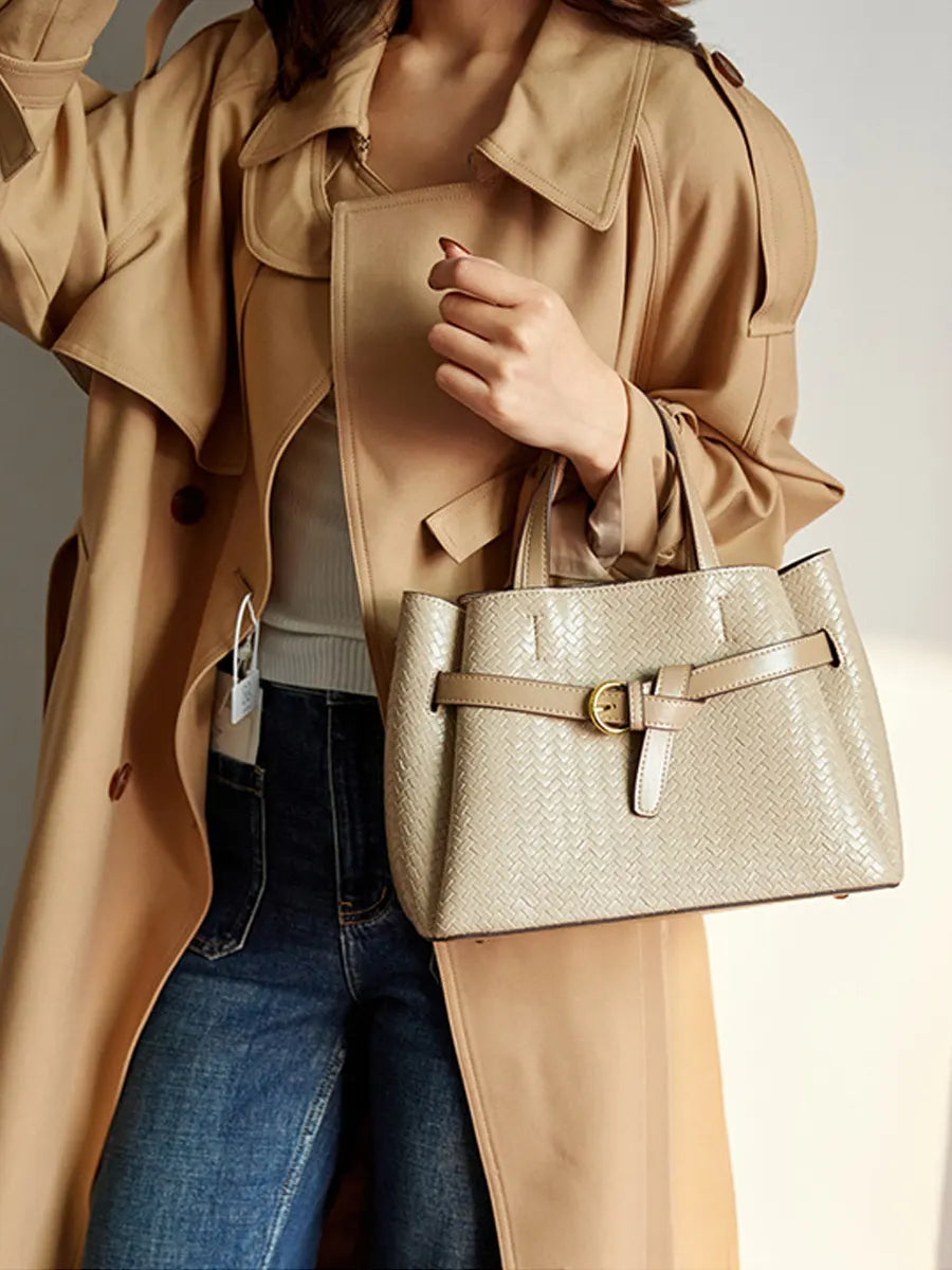 Person wearing a beige trench coat holding a matching handbag against a neutral background