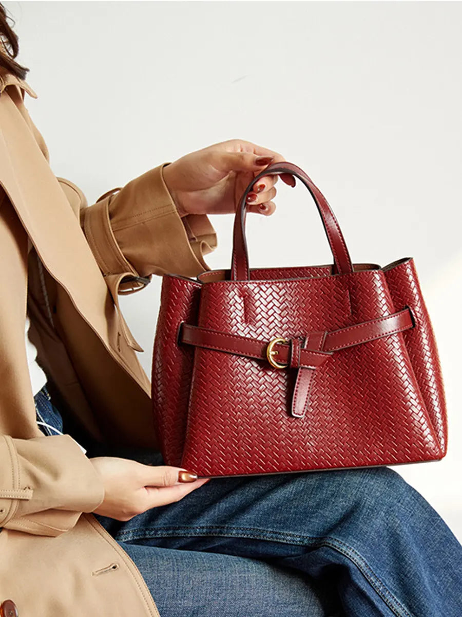 Person holding a red woven handbag with a beige coat and blue jeans on a light background