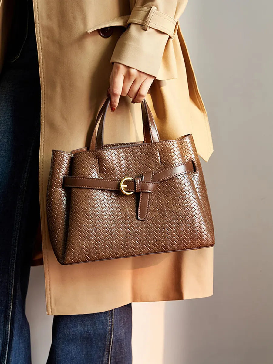 Person holding a brown woven handbag with a beige coat and blue jeans.