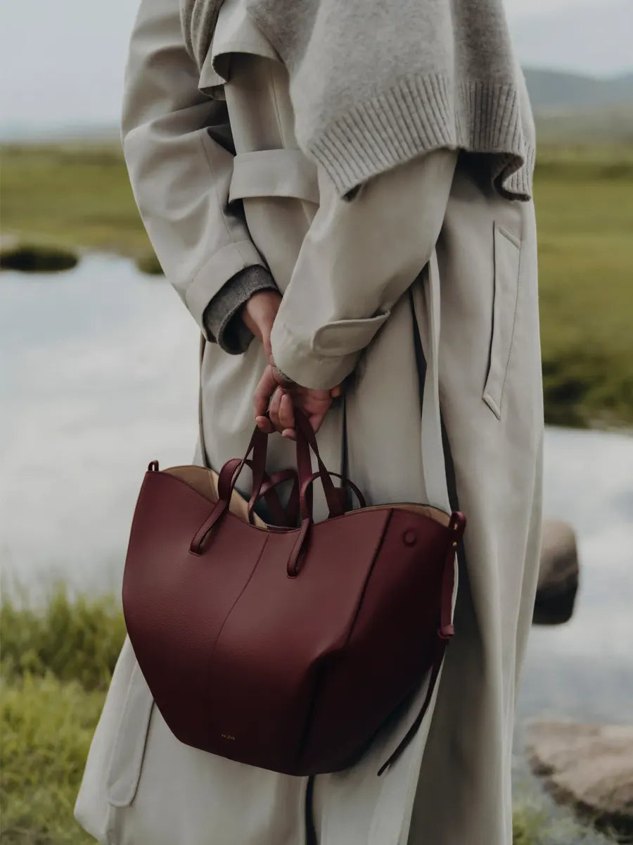 Person holding a maroon handbag in a natural setting