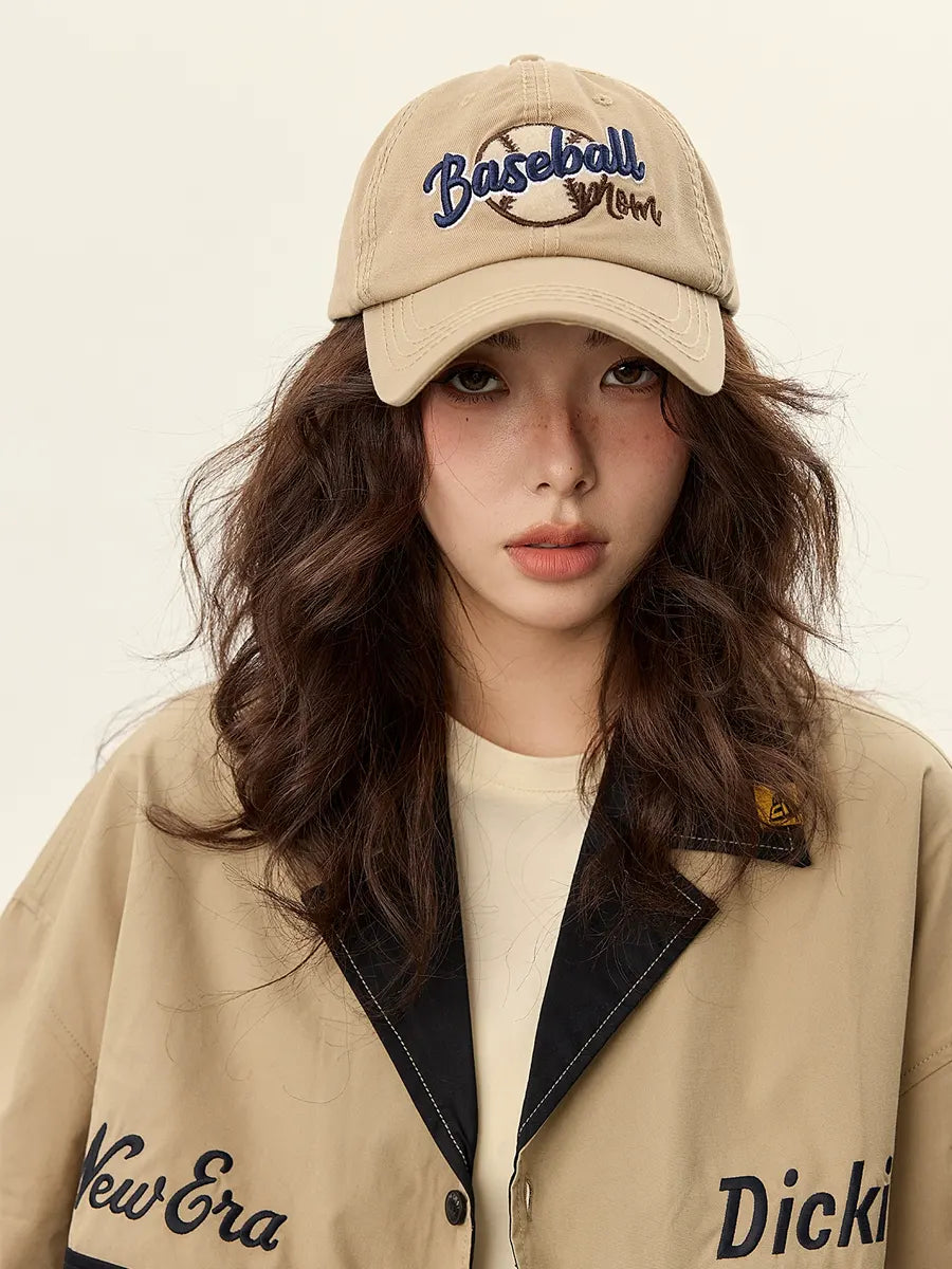 Woman wearing a beige cap with 'Baseball' text and a matching jacket on a plain background
