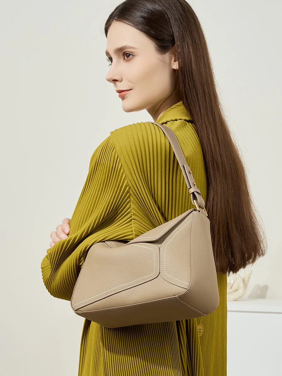 Woman in a yellow dress holding a beige handbag against a plain background