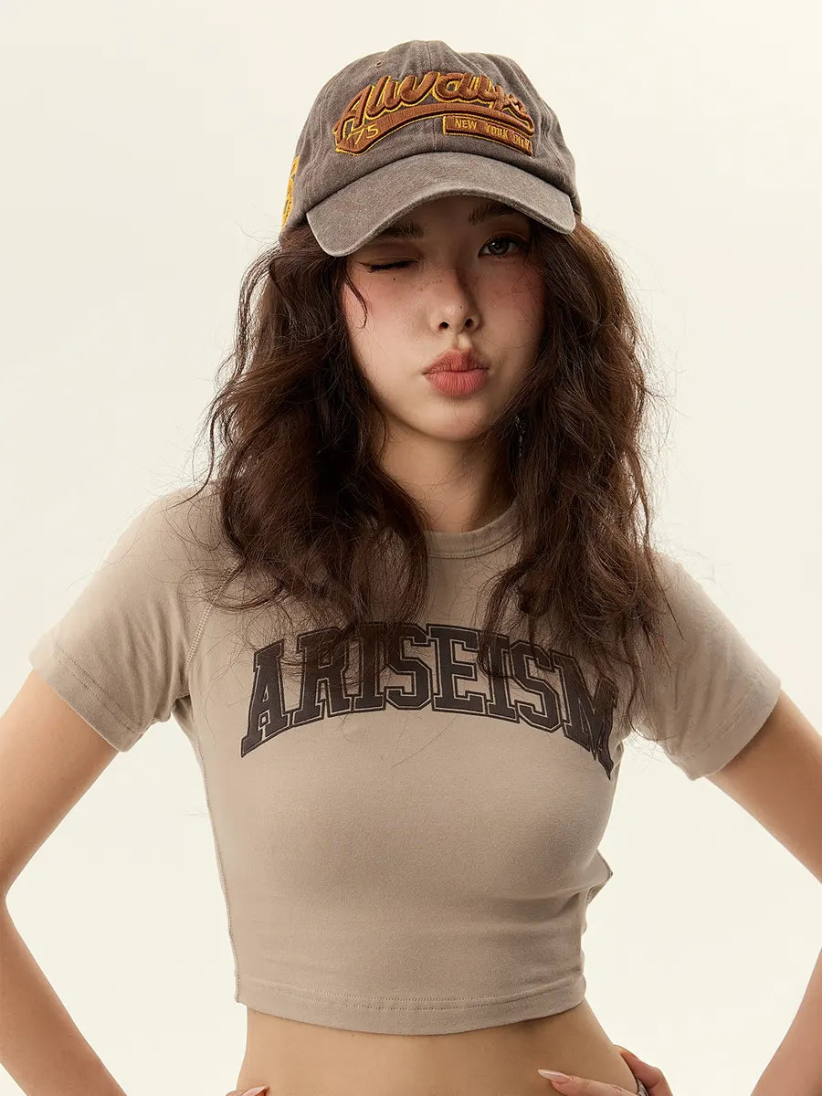 Woman wearing a beige t-shirt with text and a cap on a plain background