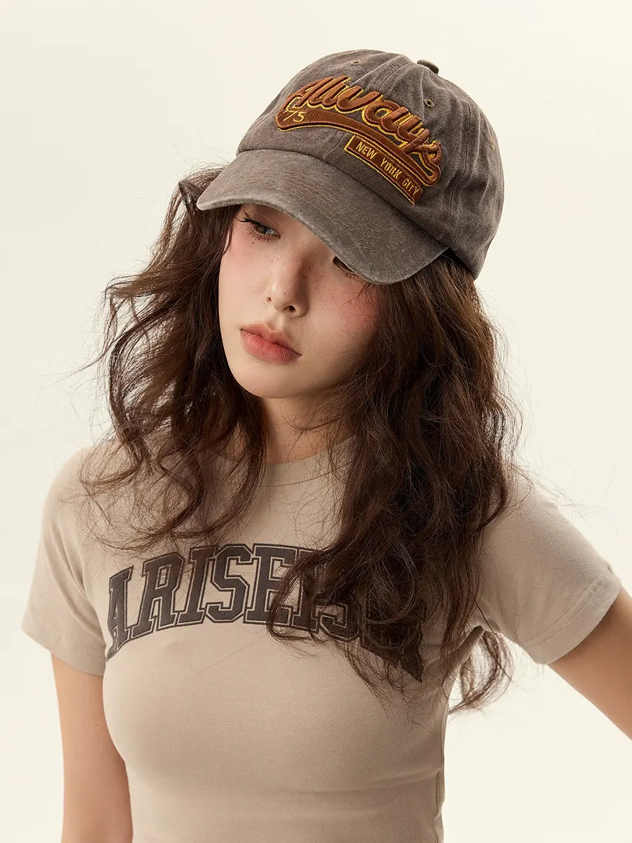 Woman wearing a gray cap and beige t-shirt with text on a plain background