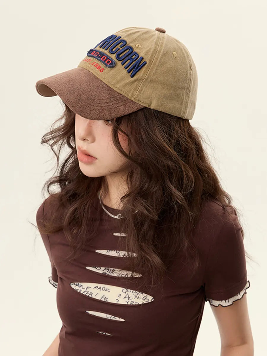 Person wearing a brown cap with 'Capricorn' text and a brown t-shirt with white designs on a beige background