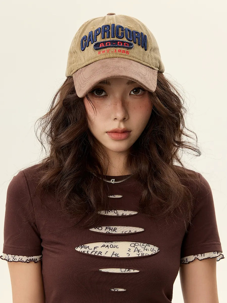 Woman wearing a cap with 'Capricorn' text and a brown t-shirt with cut-out design.