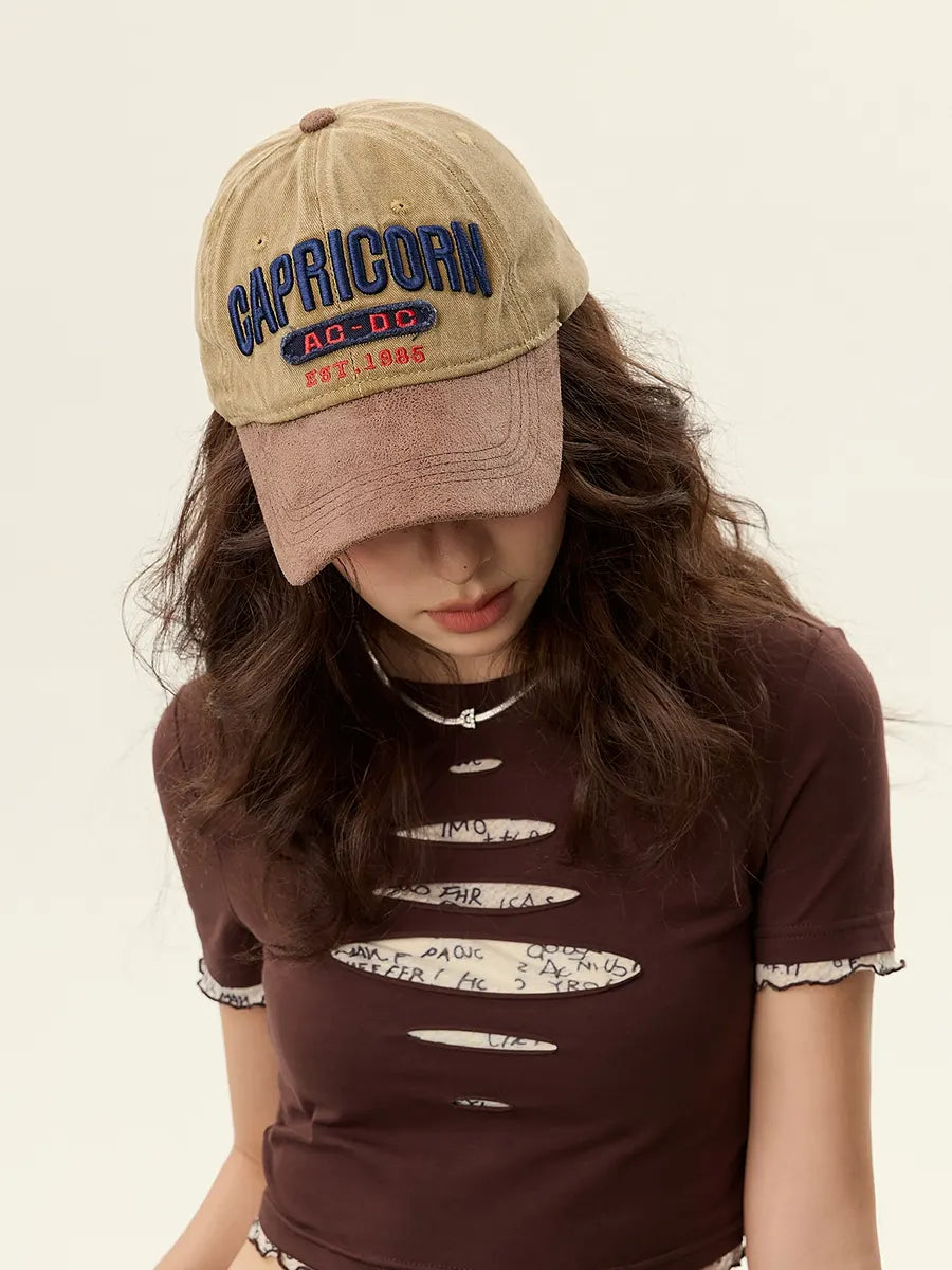 Person wearing a beige cap with 'Capricorn' text and a brown t-shirt with white text on a plain background